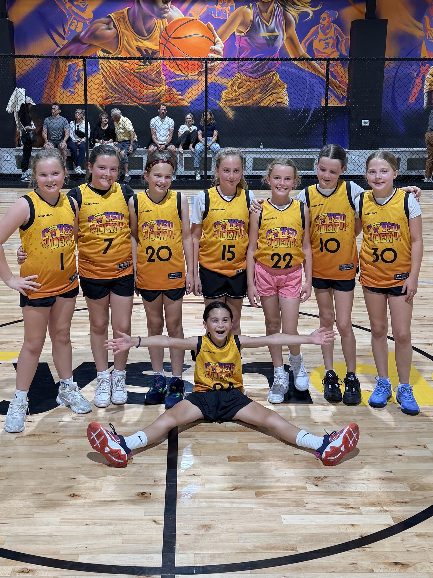 A Swysh Den girls basketball team poses together on the court after a game