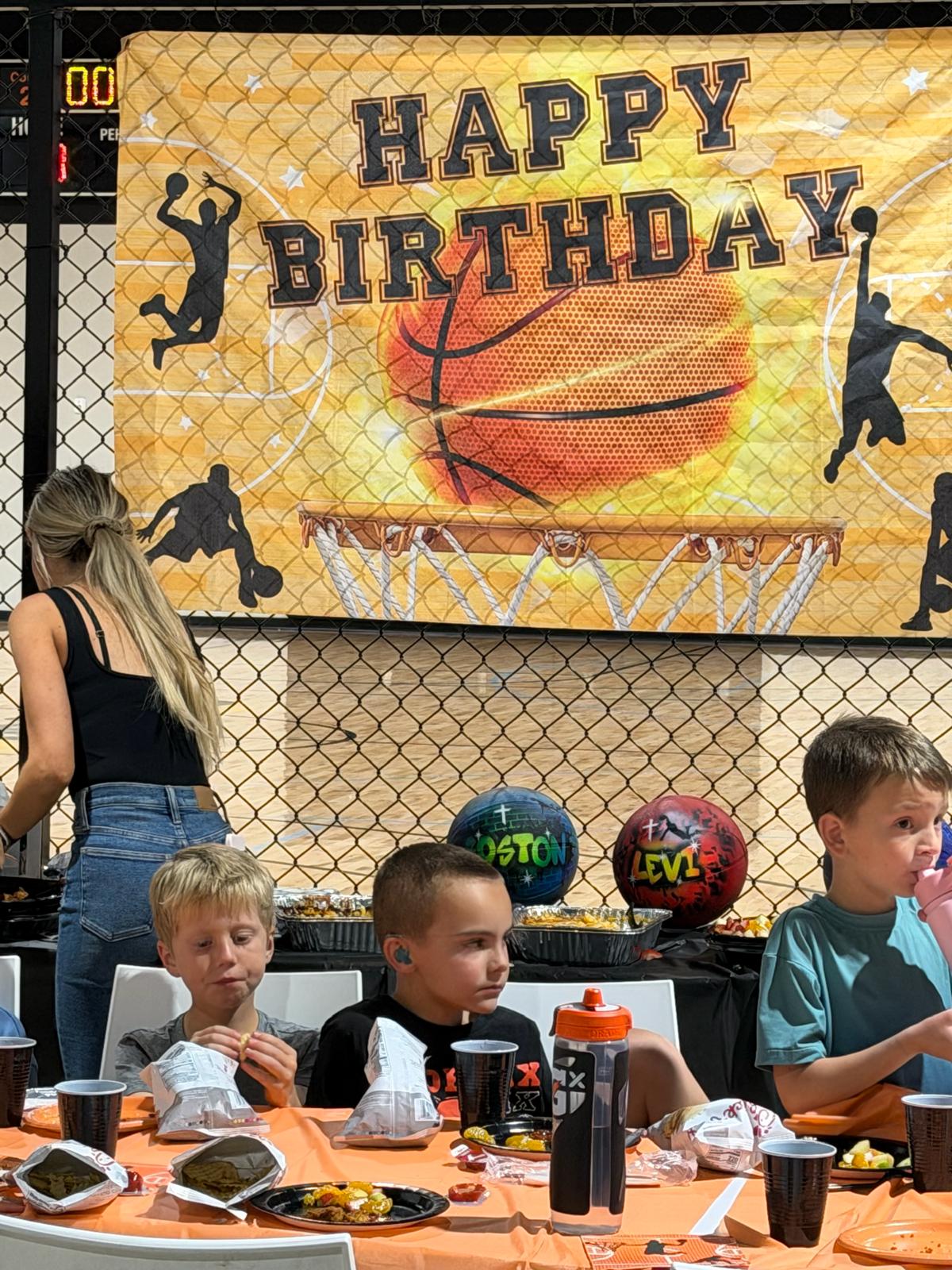 Kids eating at a table under a Happy Birthday basketball banner at a Swysh Den party