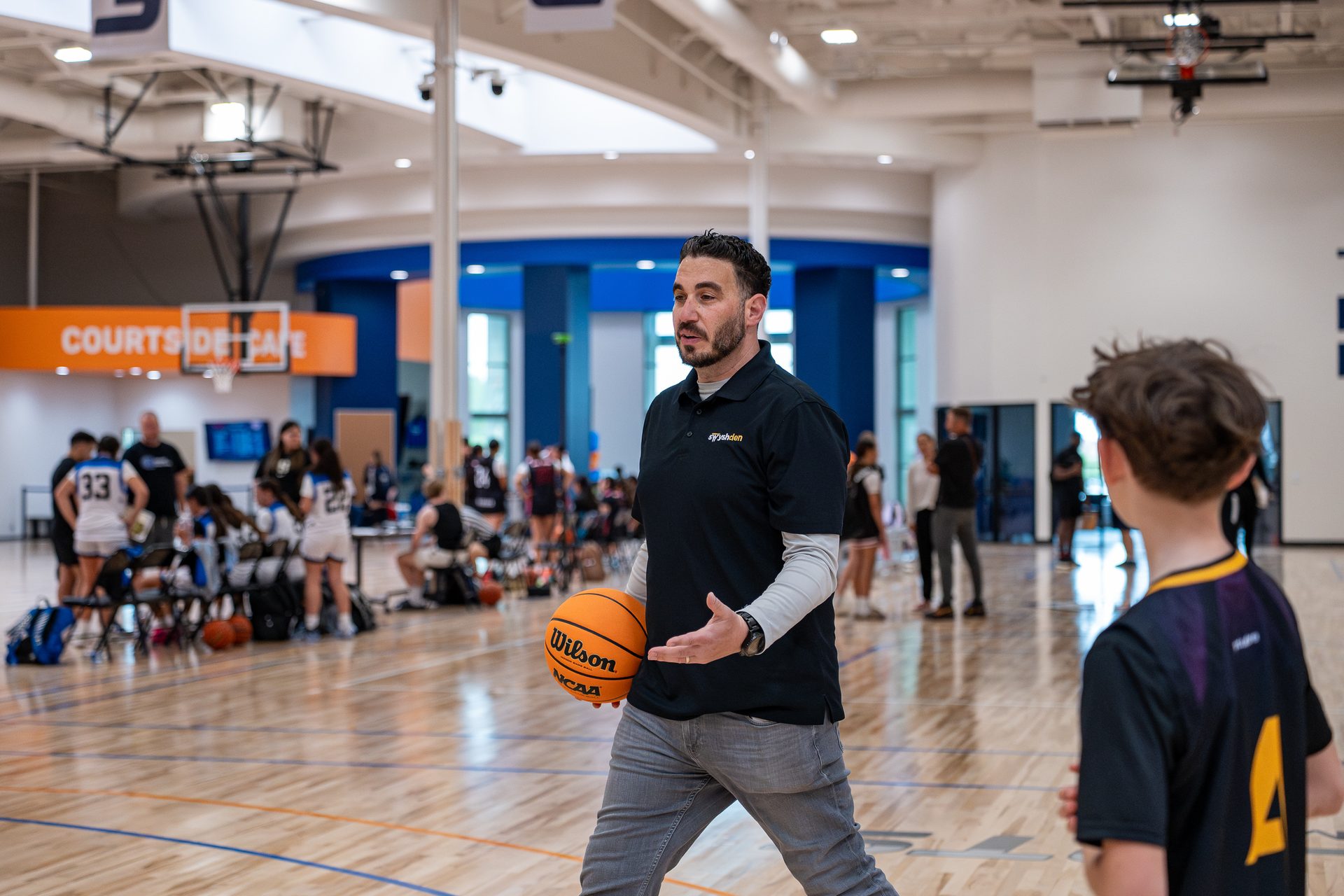 Swysh Den coach in a branded black polo working the sideline at a tournament