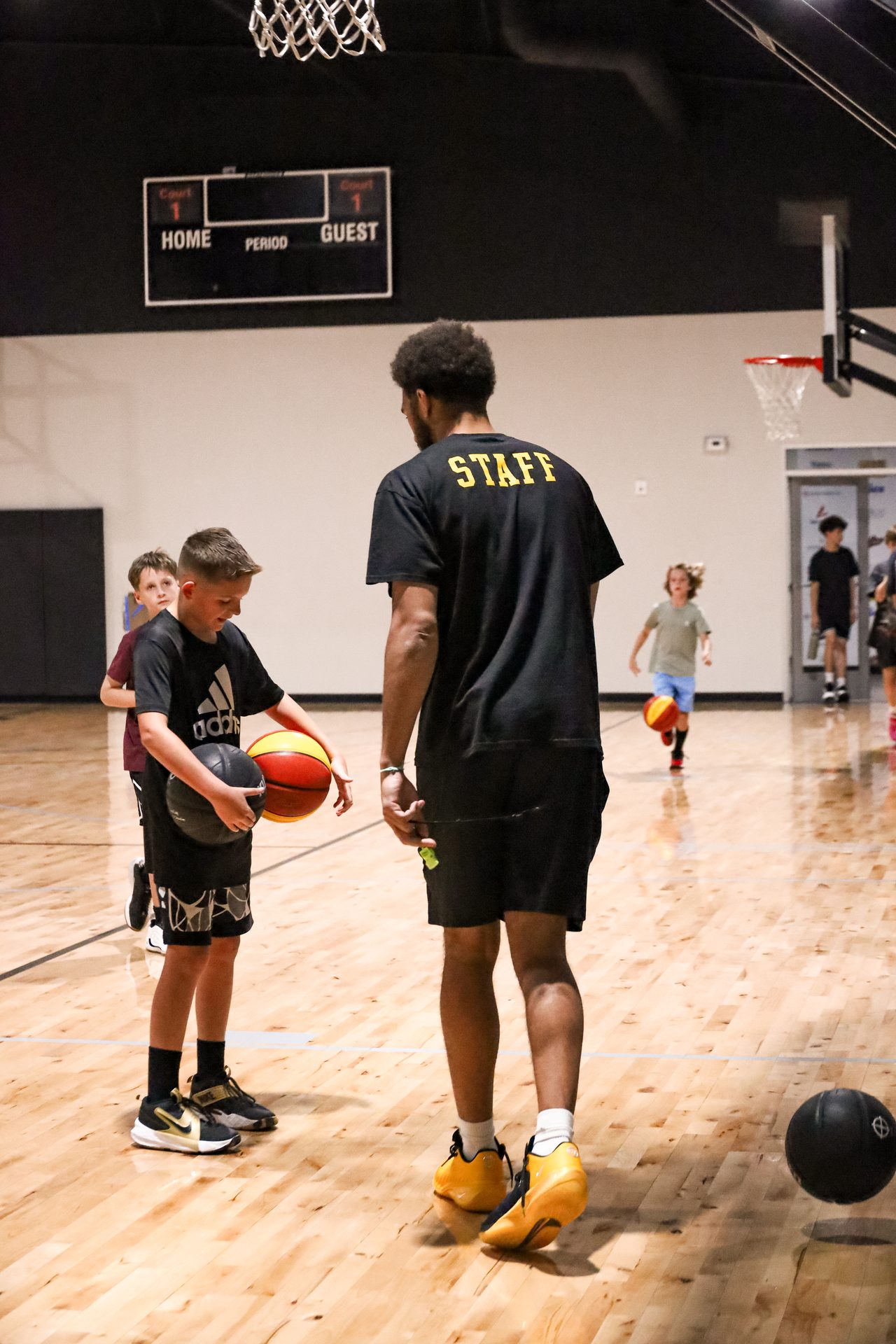 Tall Swysh Den coach in the black and gold STAFF shirt leaning down to talk with a smiling young player
