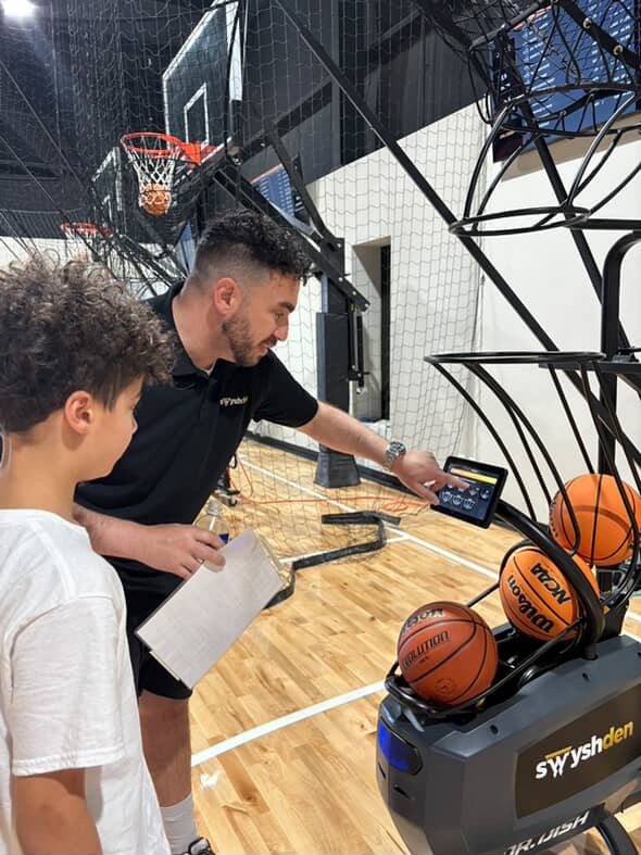 Founder Steve Moses helping a young player with a shot-training machine on the Swysh Den court