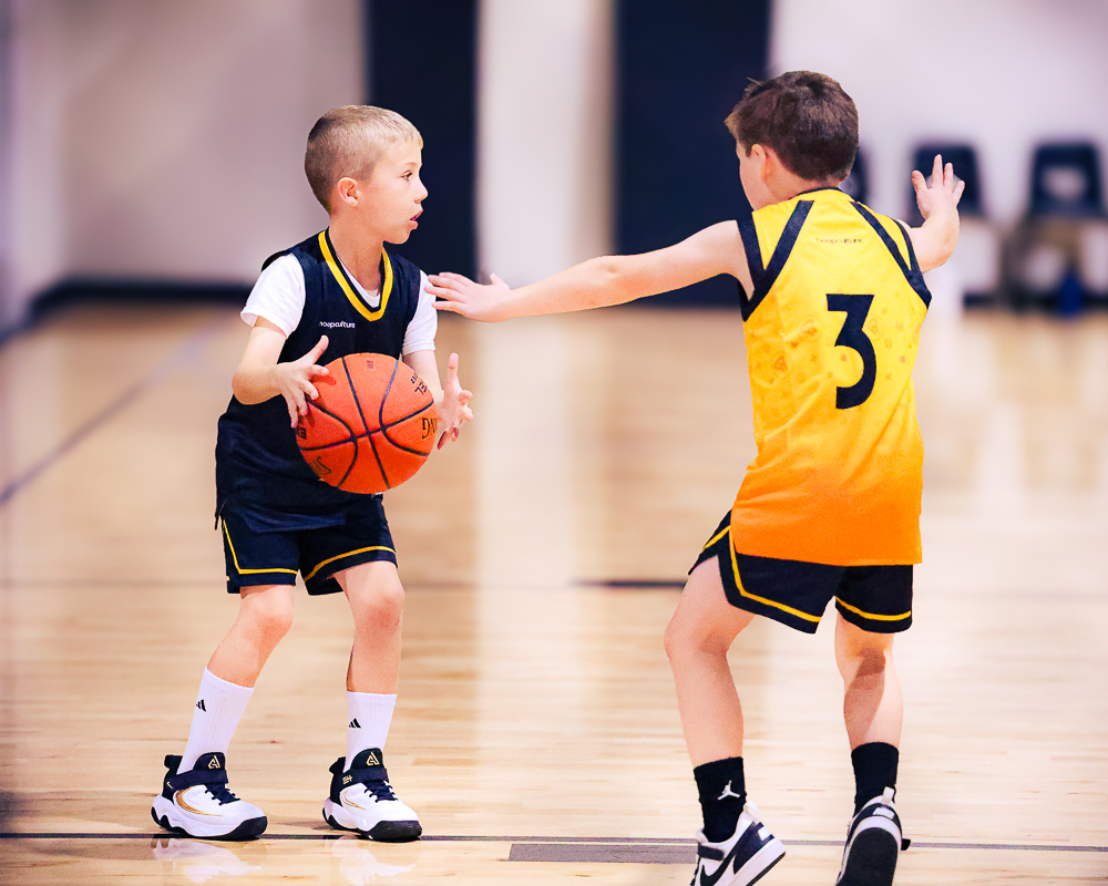 A young boy dribbles the ball while a defender reaches in at Swysh Den